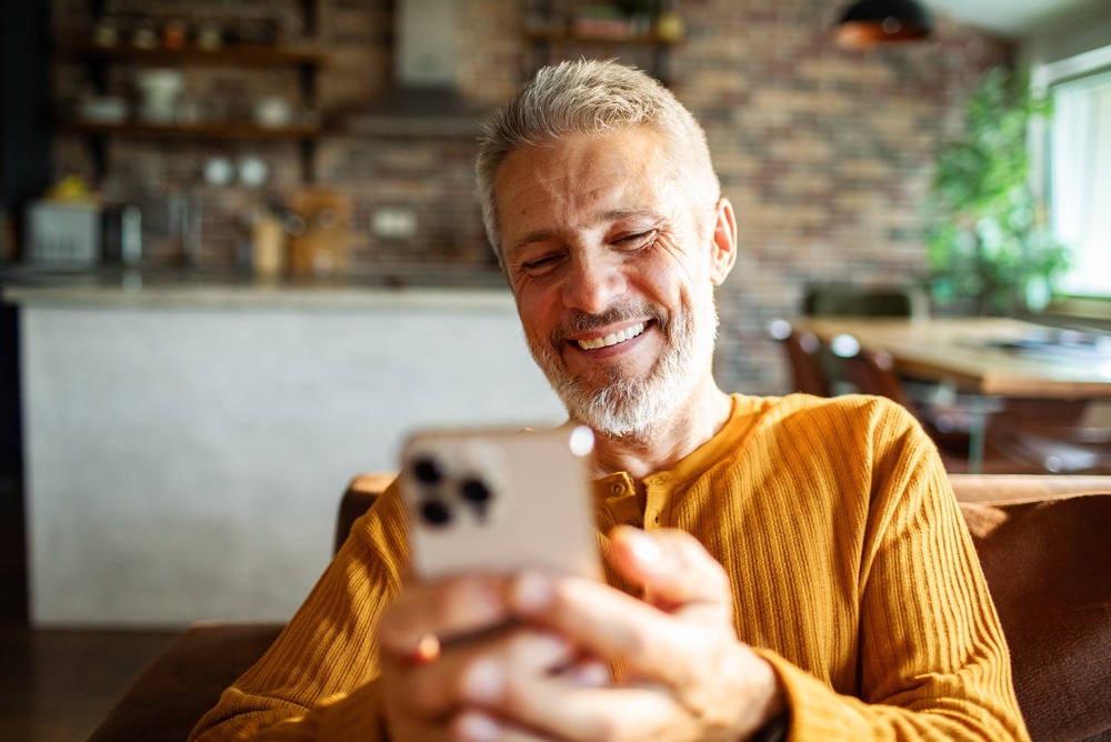 Happy mature man in kitchen at home on his phone